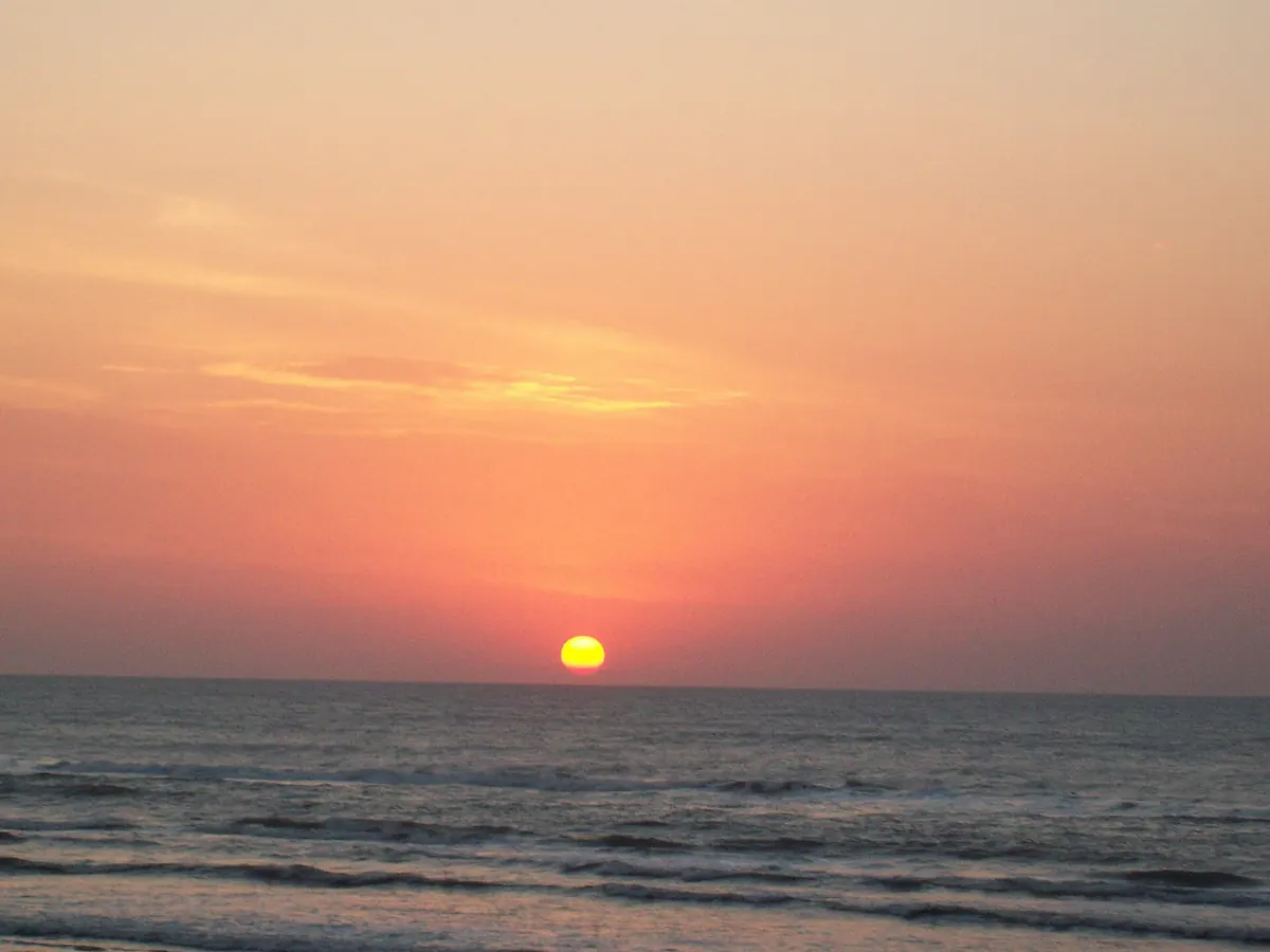 Sol baixo no horizonte sobre o mar, com céu alaranjado, em Arroio do Sal