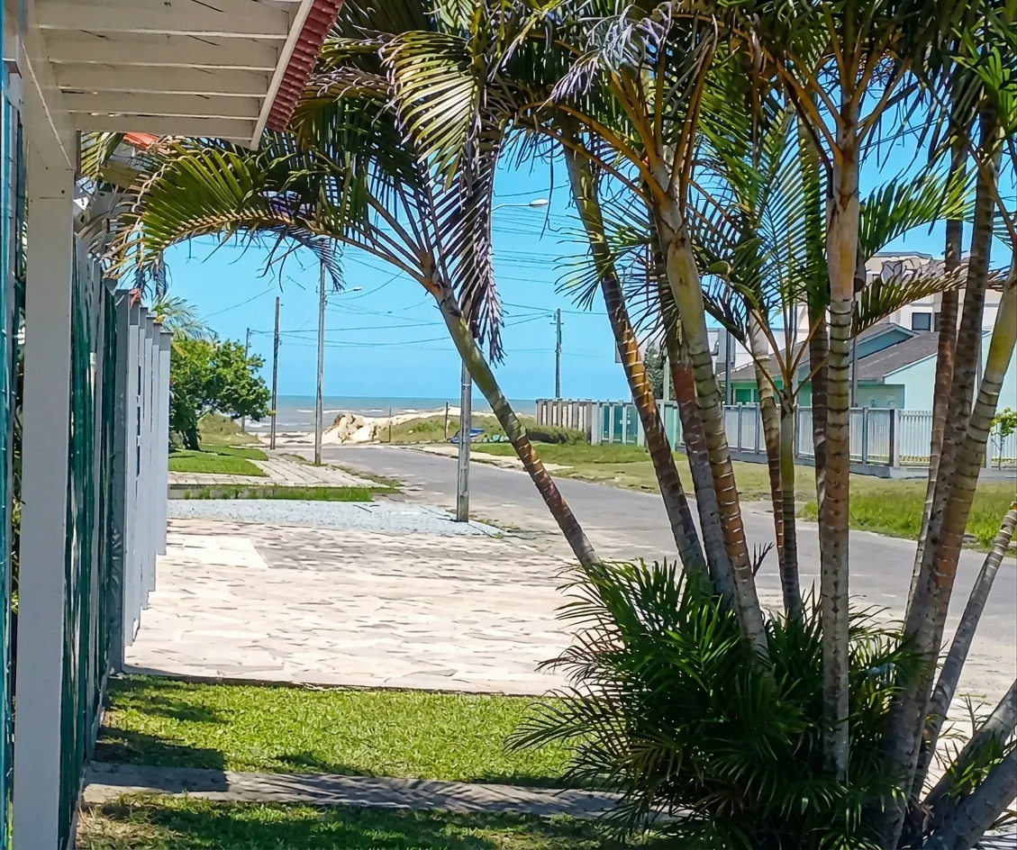 Calçada e palmeiras em frente à pousada, com a rua e o mar ao fundo